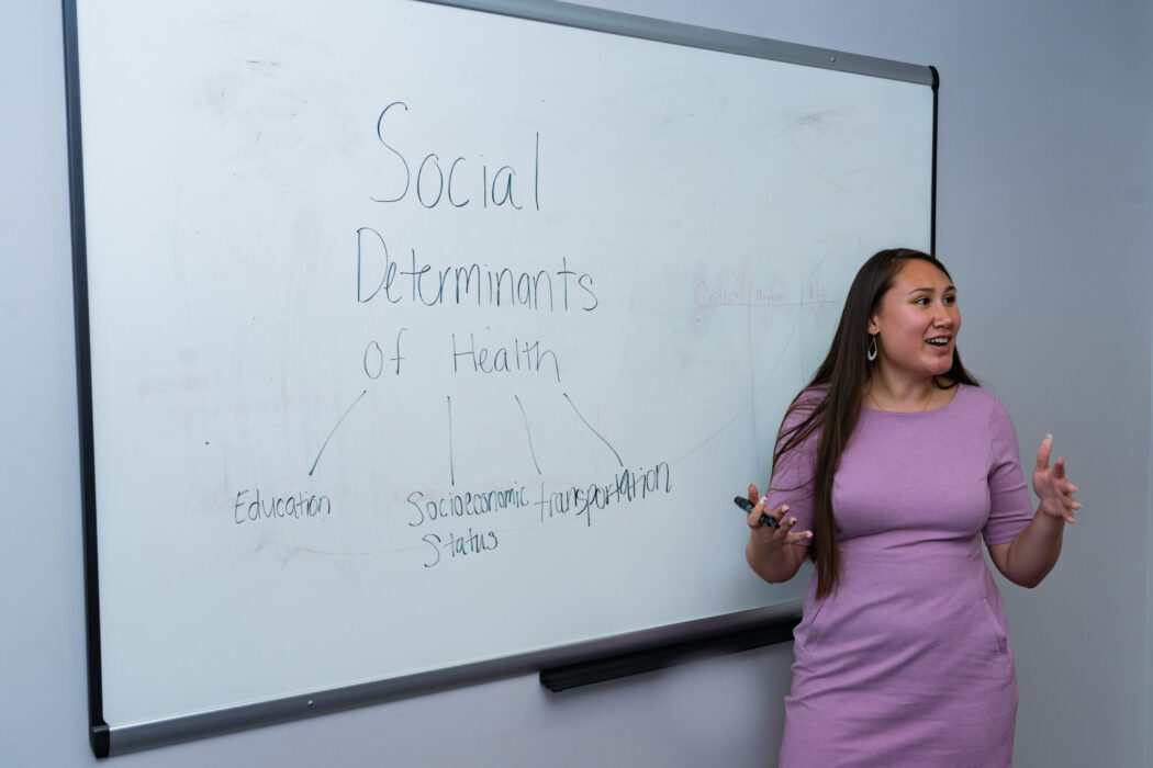 Healthy and Equitable Communities Training Woman standing in front a whiteboard teaching about the social determinants of health.
