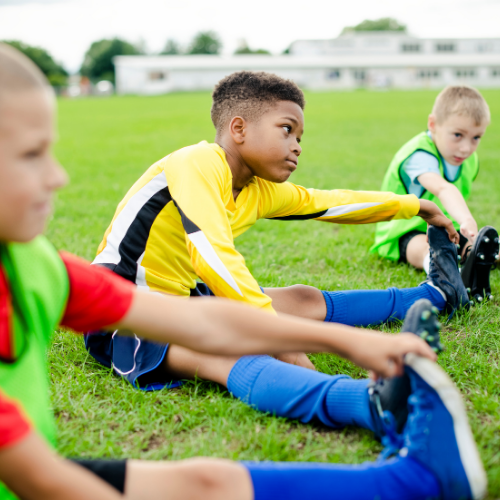 Three boys wearing soccer gear are stretching on the field.