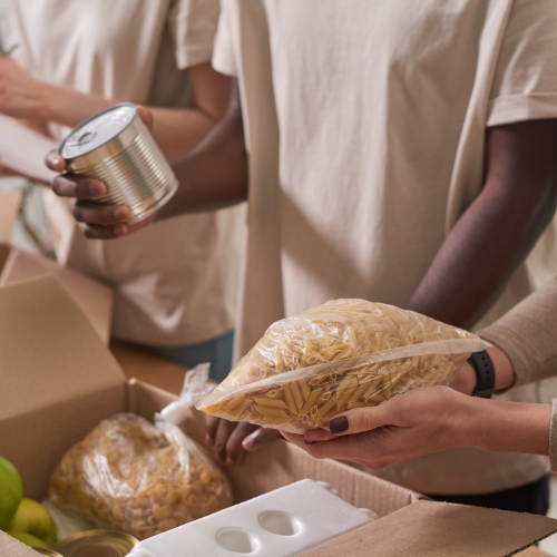 A few people wearing tan colored shirts are packing boxes with food donations.