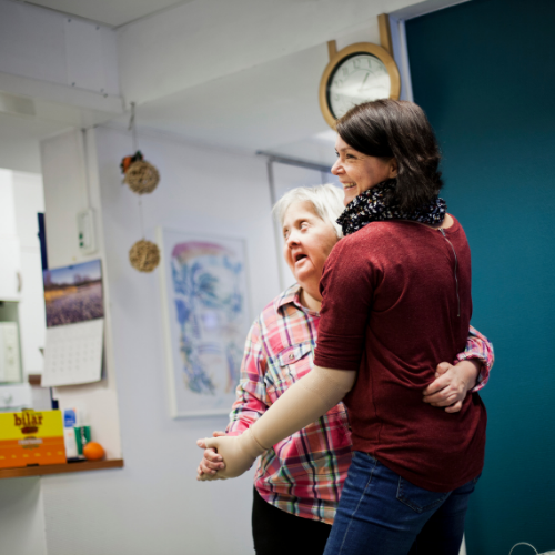 Woman with burgundy shirt dancing in hospital with patient with down syndrome.