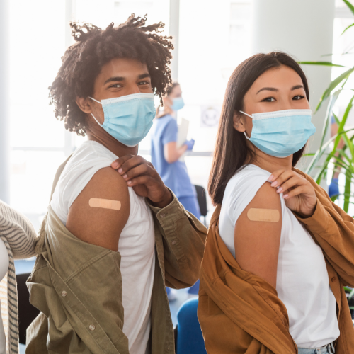 A few people wearing masks are showing off their bandaids after receiving a vaccine.