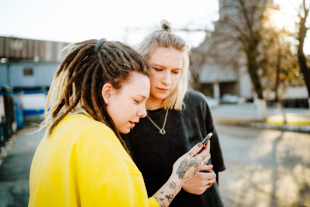 Two androgynous women looking at a phone together.