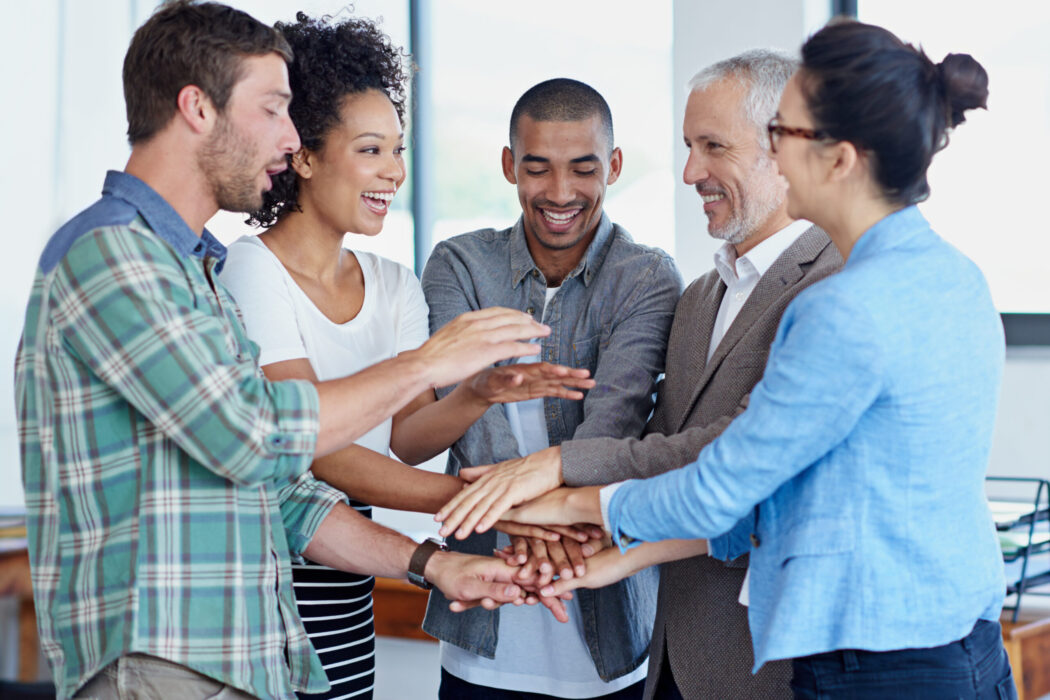 shot-of-a-group-of-happy-coworkers-standing-with-t-2023-01-04-20-30-36-utc Shot of a group of happy coworkers standing with their hands together in huddle in an office.