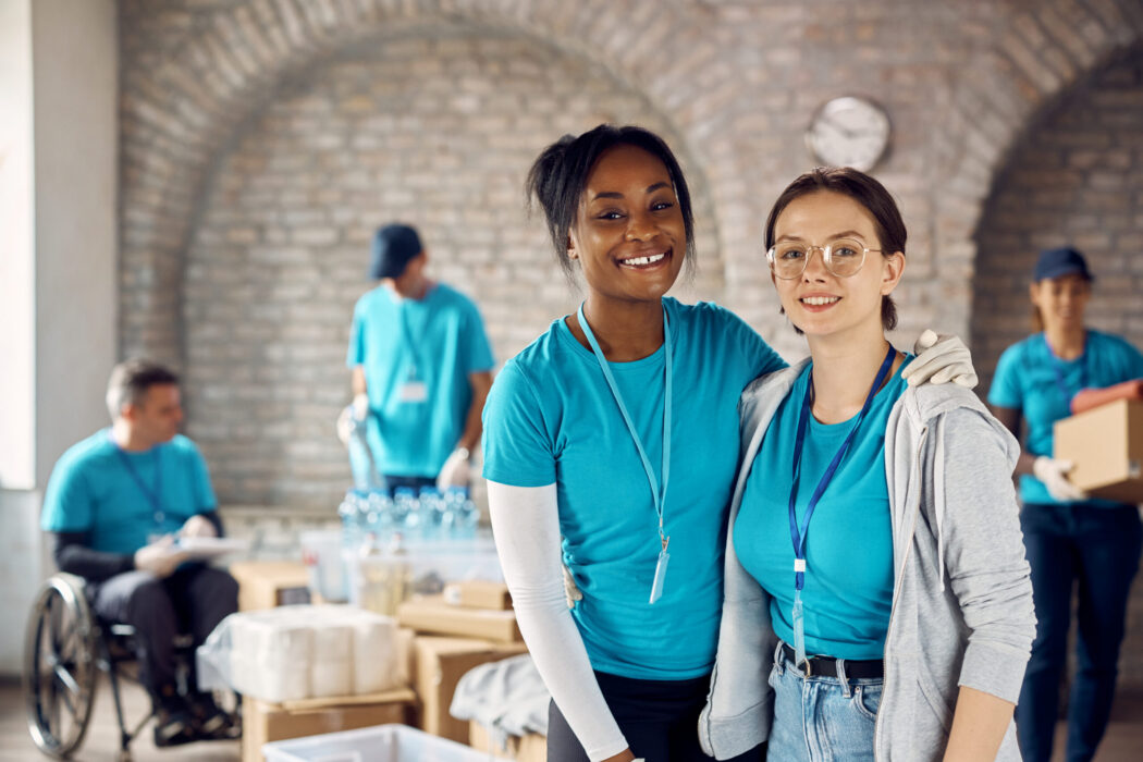 African American woman and her Caucasian friend working as volunteers at humanitarian aid center and looking at camera.